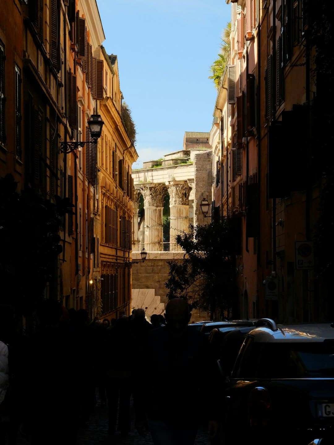 Persone camminano lungo uno stretto vicolo acciottolato verso antiche rovine romane.