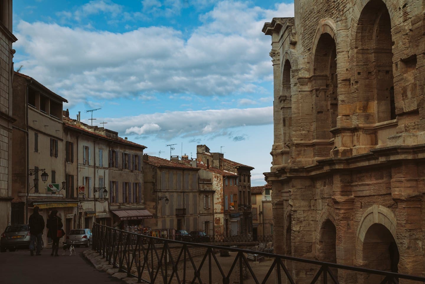 Persone e cane passeggiano lungo una strada storica con architettura romana.
